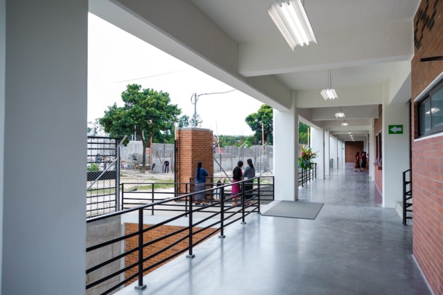 A modern corridor with bright lights, overlooking a fenced construction site, with people standing and working nearby.