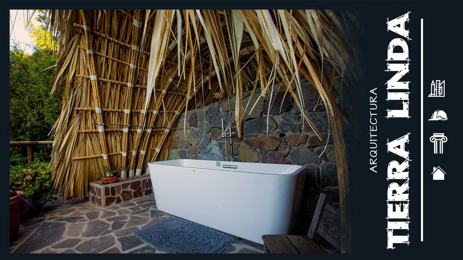 A modern white bathtub set in a rustic outdoor space with stone walls and a thatched roof, surrounded by lush greenery.