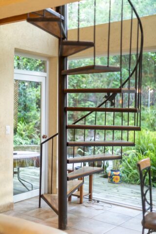 Interior view of a spiral staircase with a patio visible through a nearby window, featuring outdoor furniture.